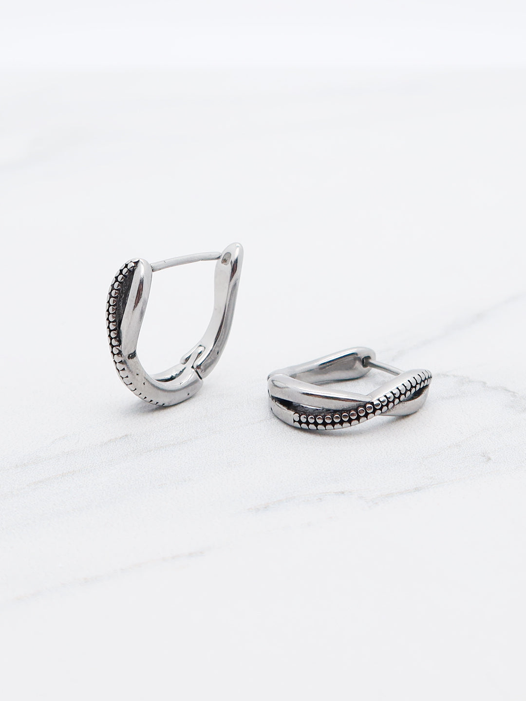 Twisted beaded huggie earrings made of titanium with a polished silver-tone finish, featuring a secure hinged snap closure.