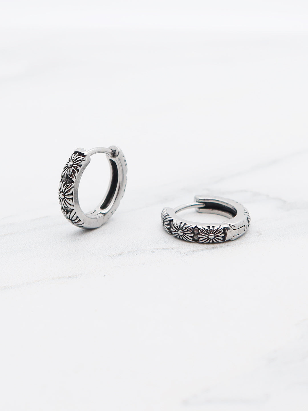 Close-up view of daisy-patterned hoop earrings with hinged clasp